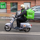 A delivery driver rides a motorized scooter with a large, green, Uber-branded backpack on.